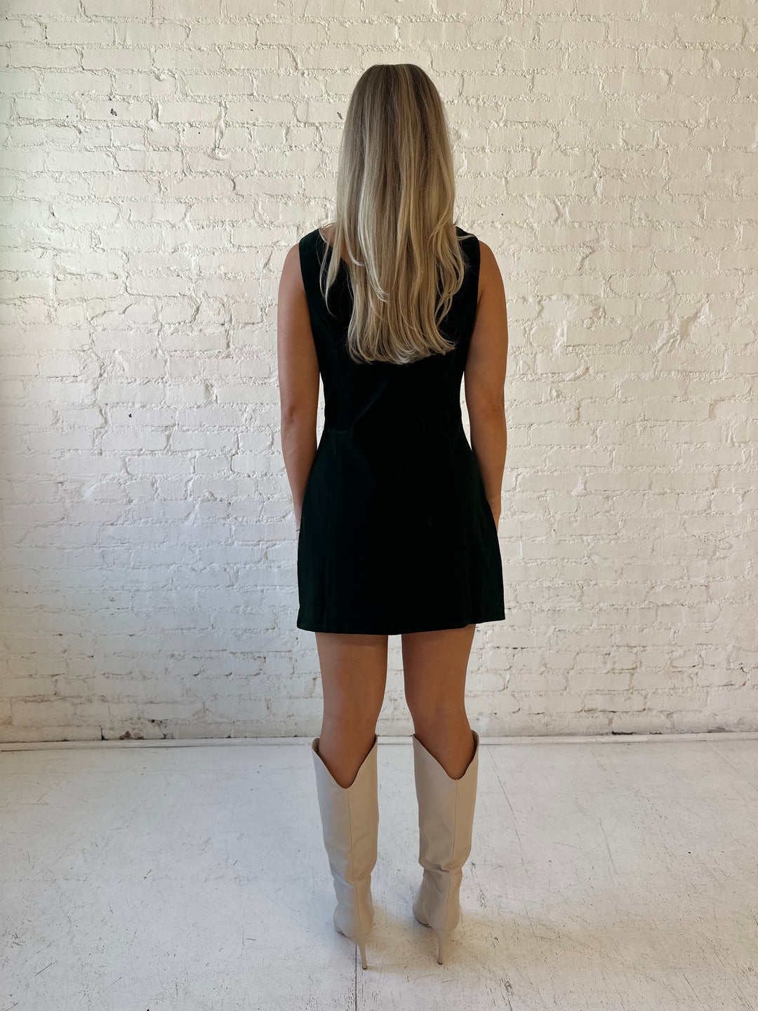 Woman wearing dark green velvet A-line mini dress with high neckline, and v-back. 