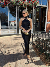 Woman wearing black satin maxi dress with halter neckline. 