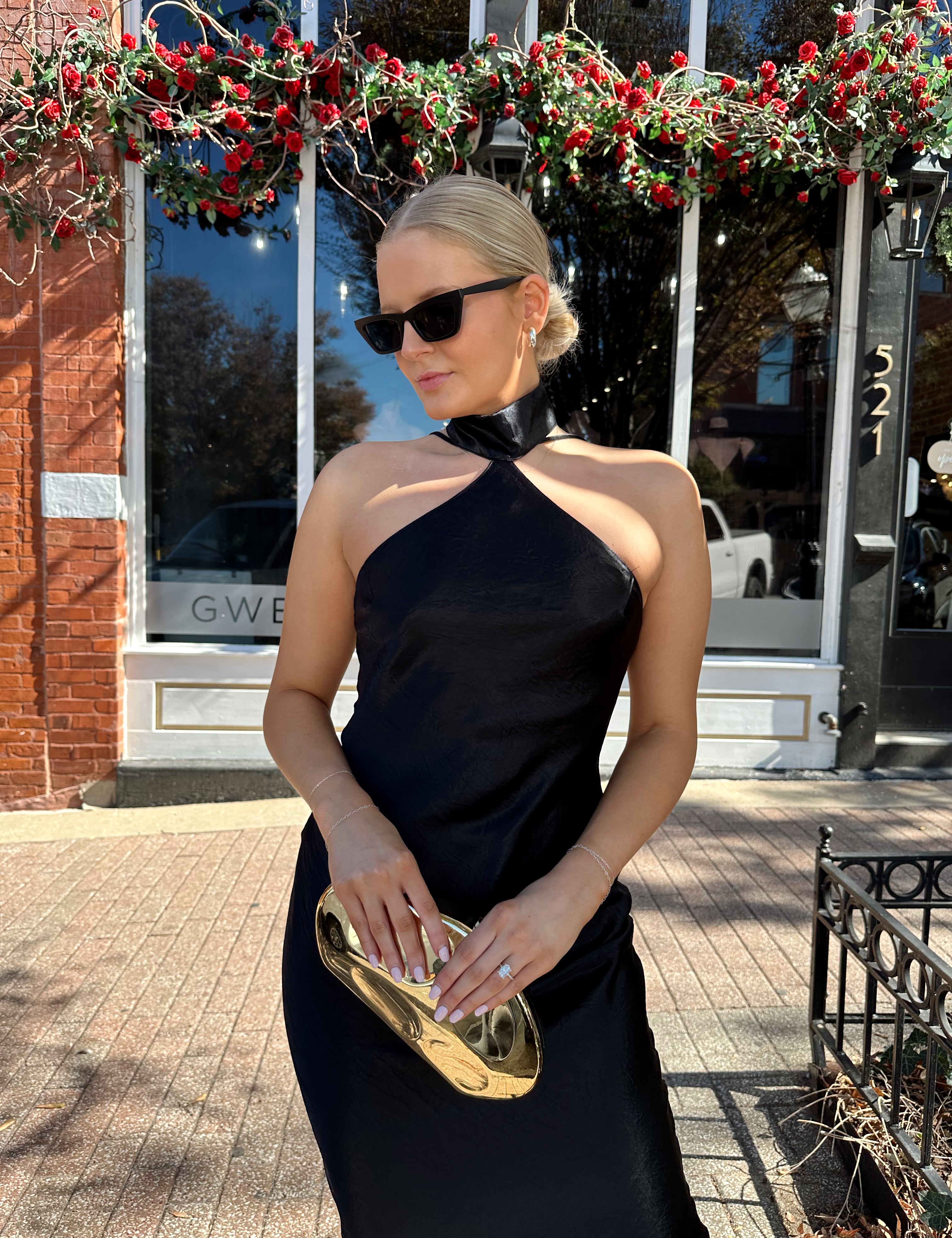 Woman wearing black satin maxi dress with halter neckline. 