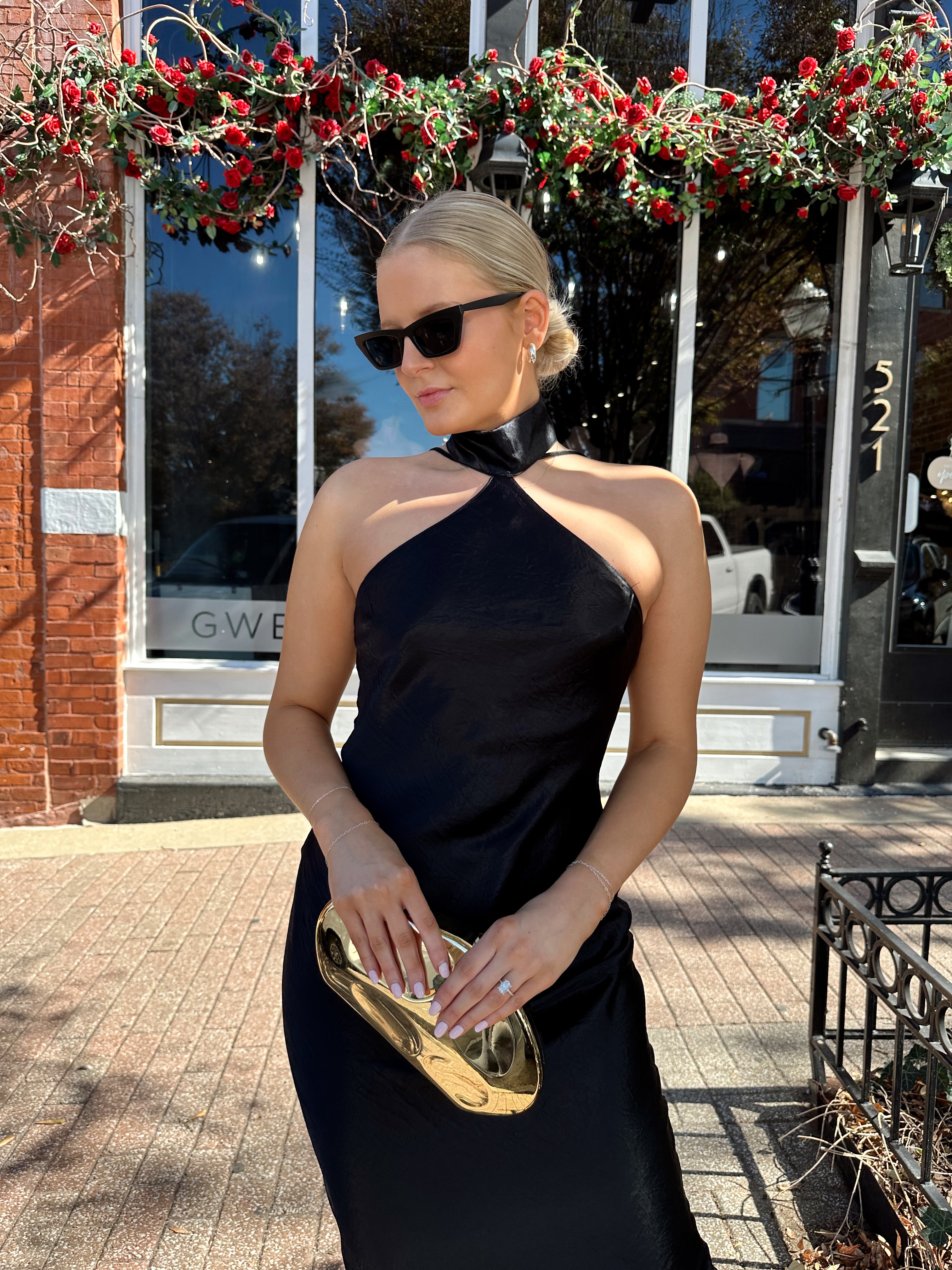 Woman wearing black satin maxi dress with halter neckline. 