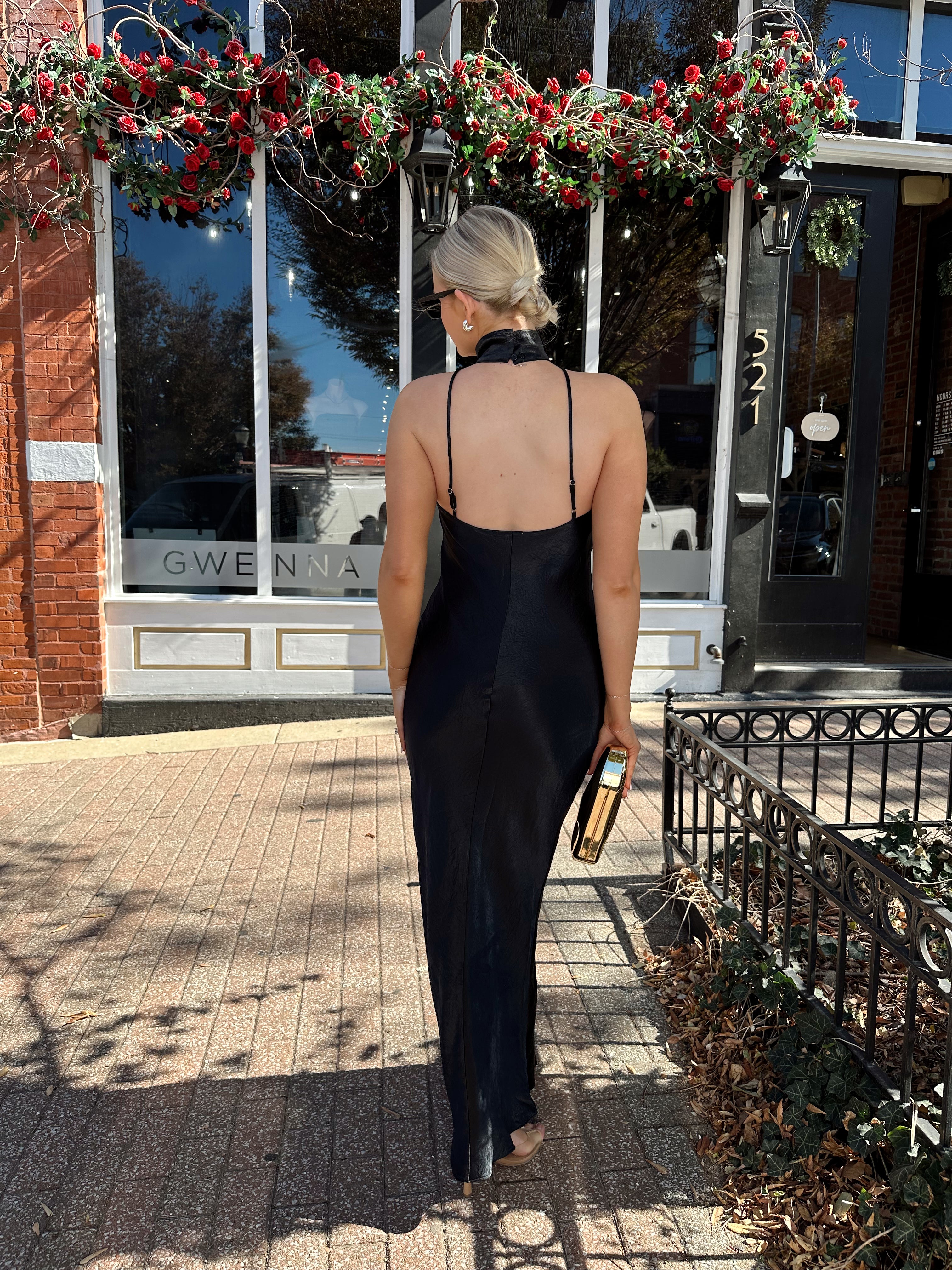 Woman wearing black satin maxi dress with halter neckline. 