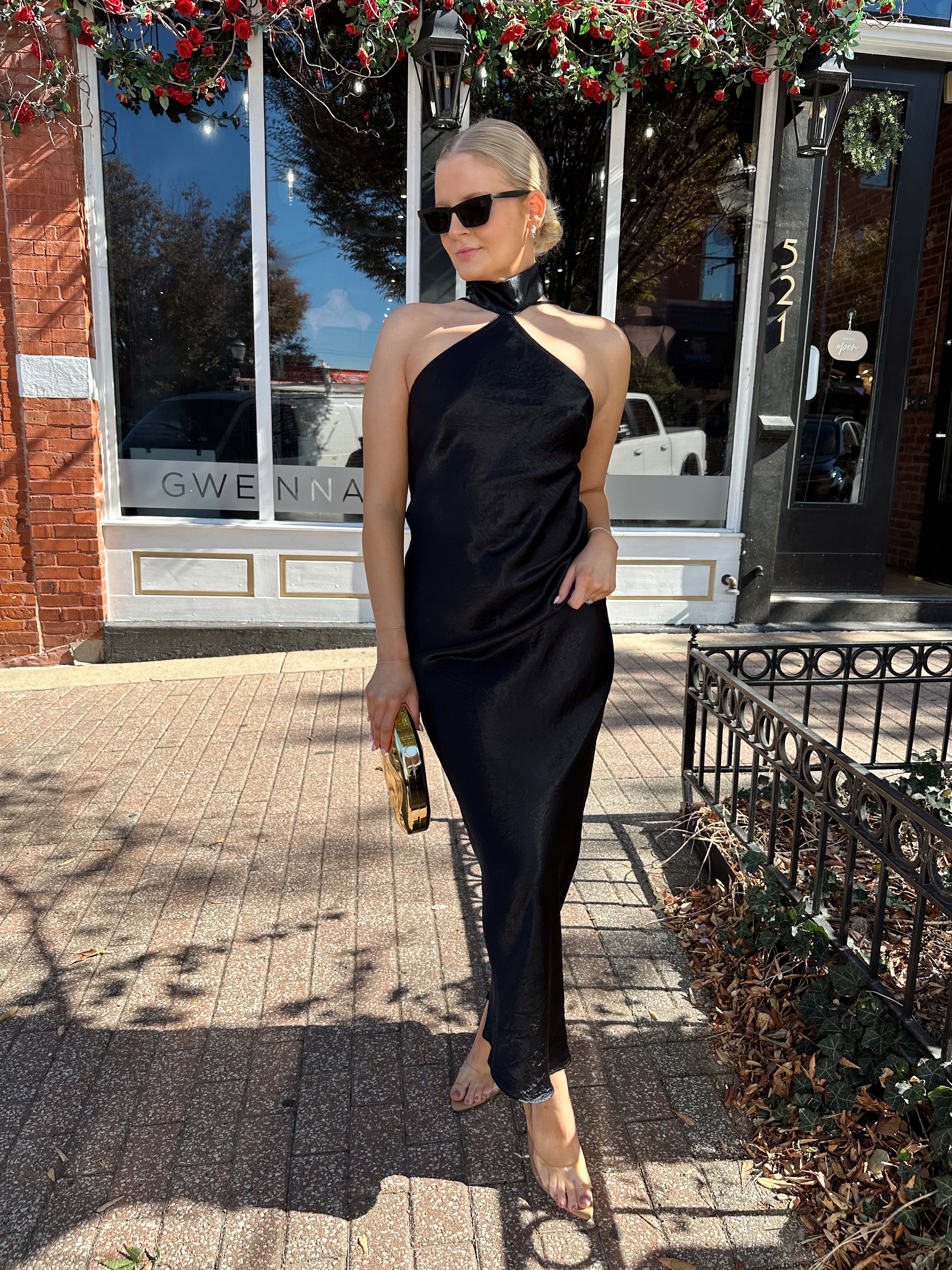 Woman wearing black satin maxi dress with halter neckline. 
