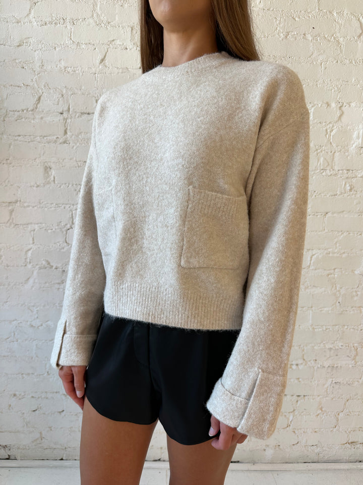 Woman wearing taupe knit sweater with front pockets, little wrist detailing, and faux leather shorts. 