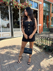 Woman wearing black strapless two piece set with mini skort and gold button detailing.