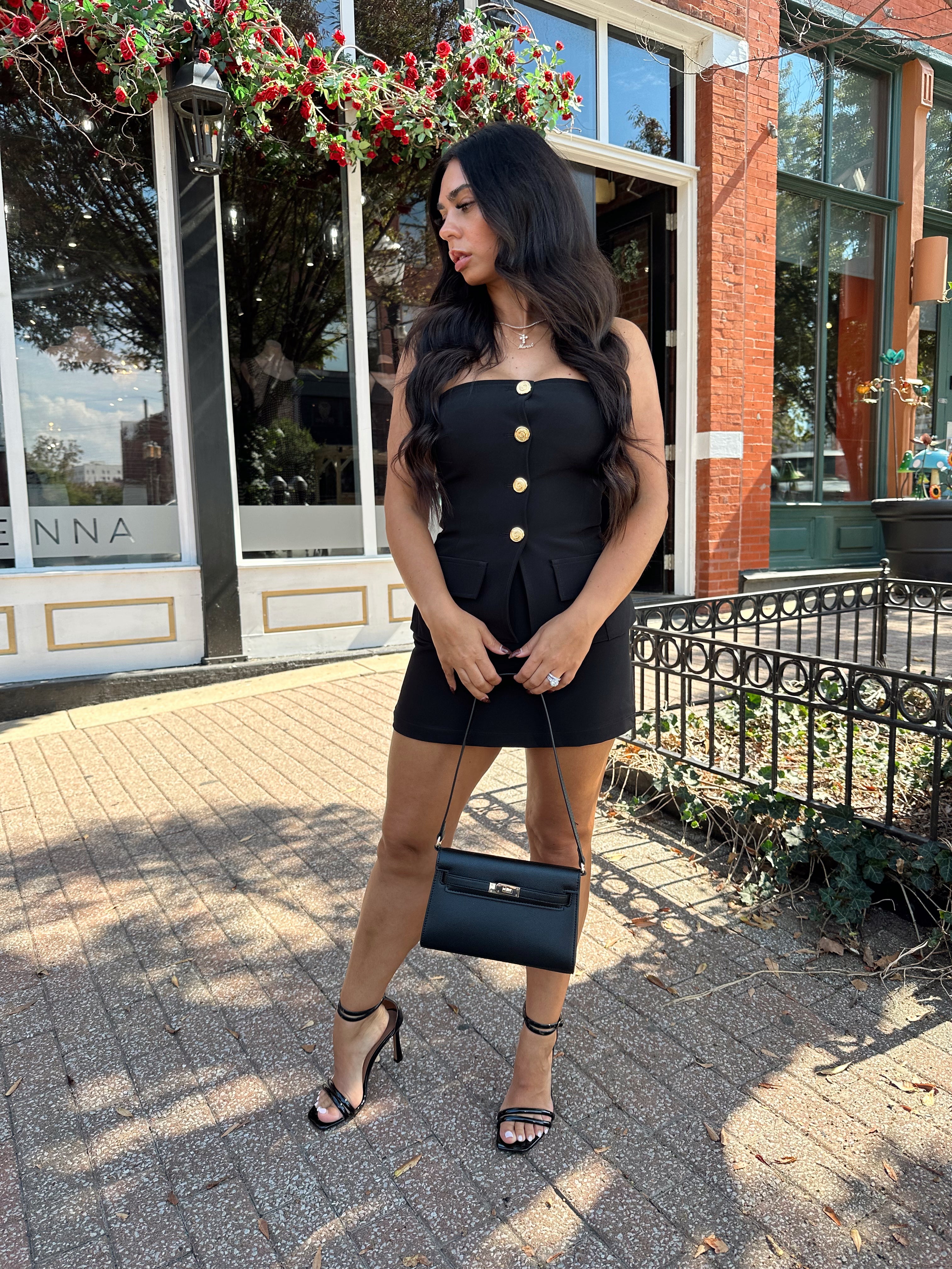 Woman wearing black strapless two piece set with mini skort and gold button detailing.