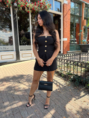 Woman wearing black strapless two piece set with mini skort and gold button detailing.