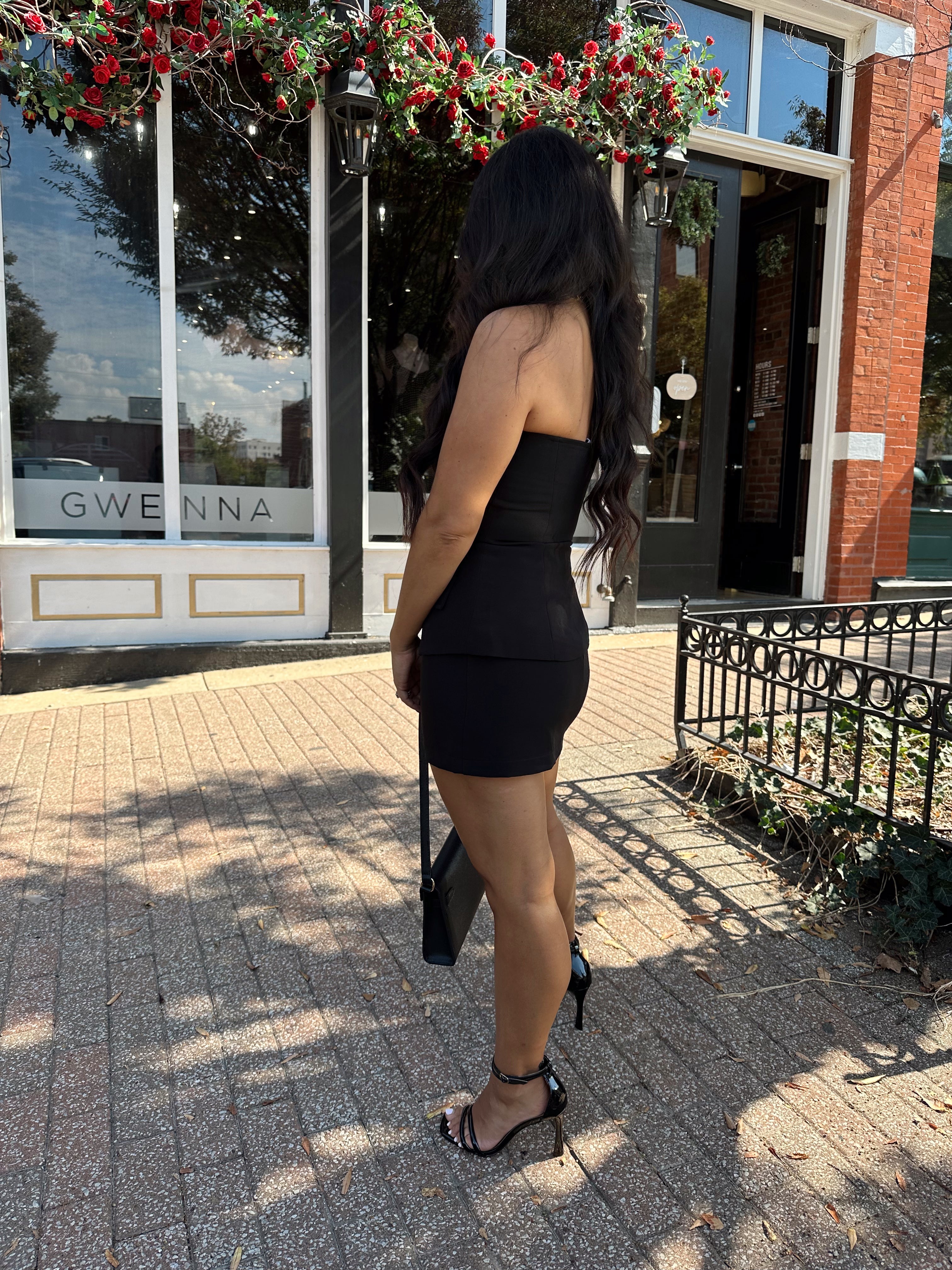 Woman wearing black strapless two piece set with mini skort and gold button detailing.