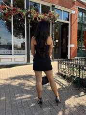 Woman wearing black strapless two piece set with mini skort and gold button detailing.