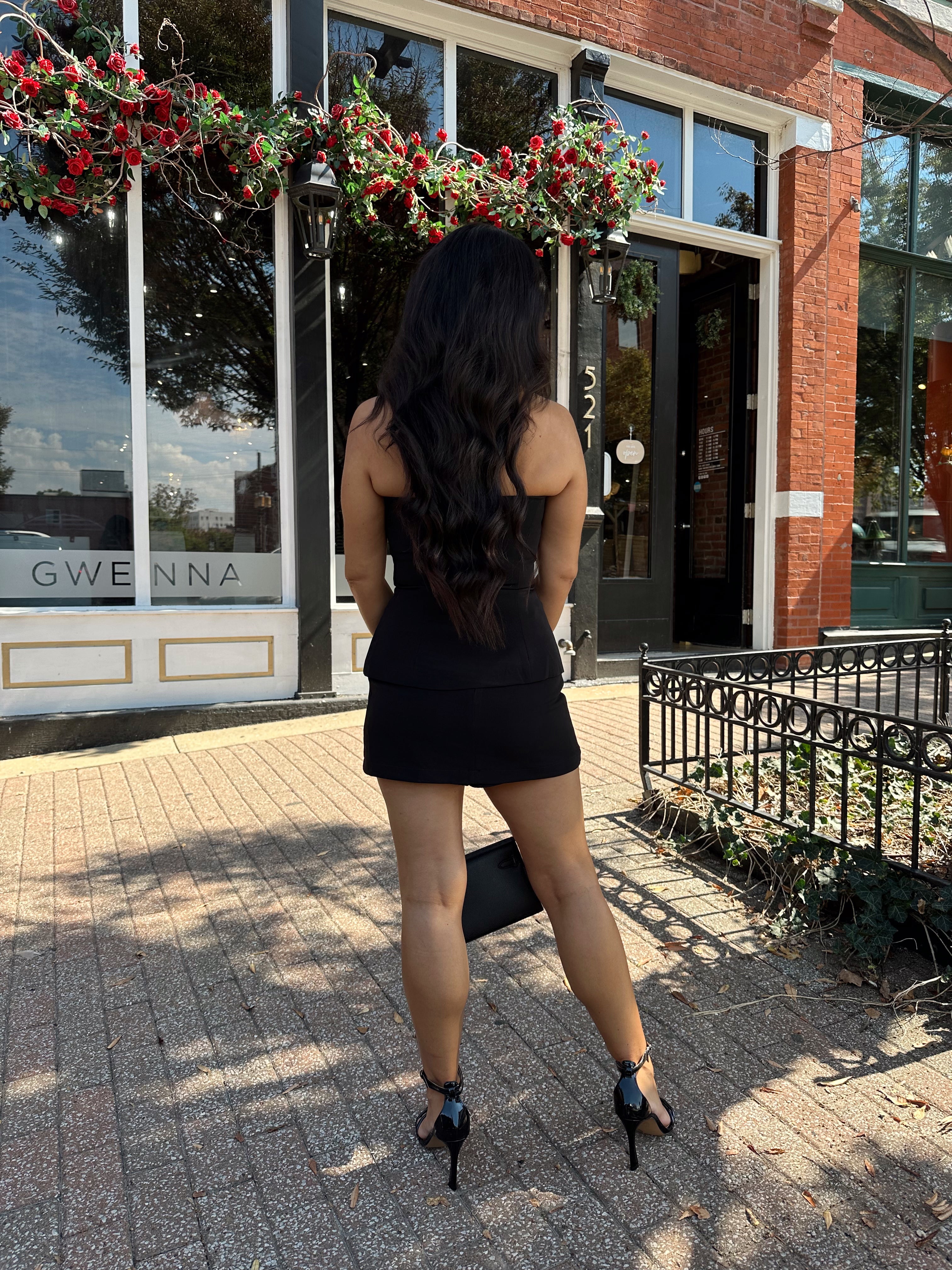 Woman wearing black strapless two piece set with mini skort and gold button detailing.