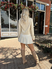 Woman wearing a light beige faux leather jacket with gold button closure. 