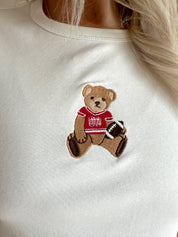 Woman wearing a white cropped t-shirt with embroidered teddy bear and cream mini skirt. 