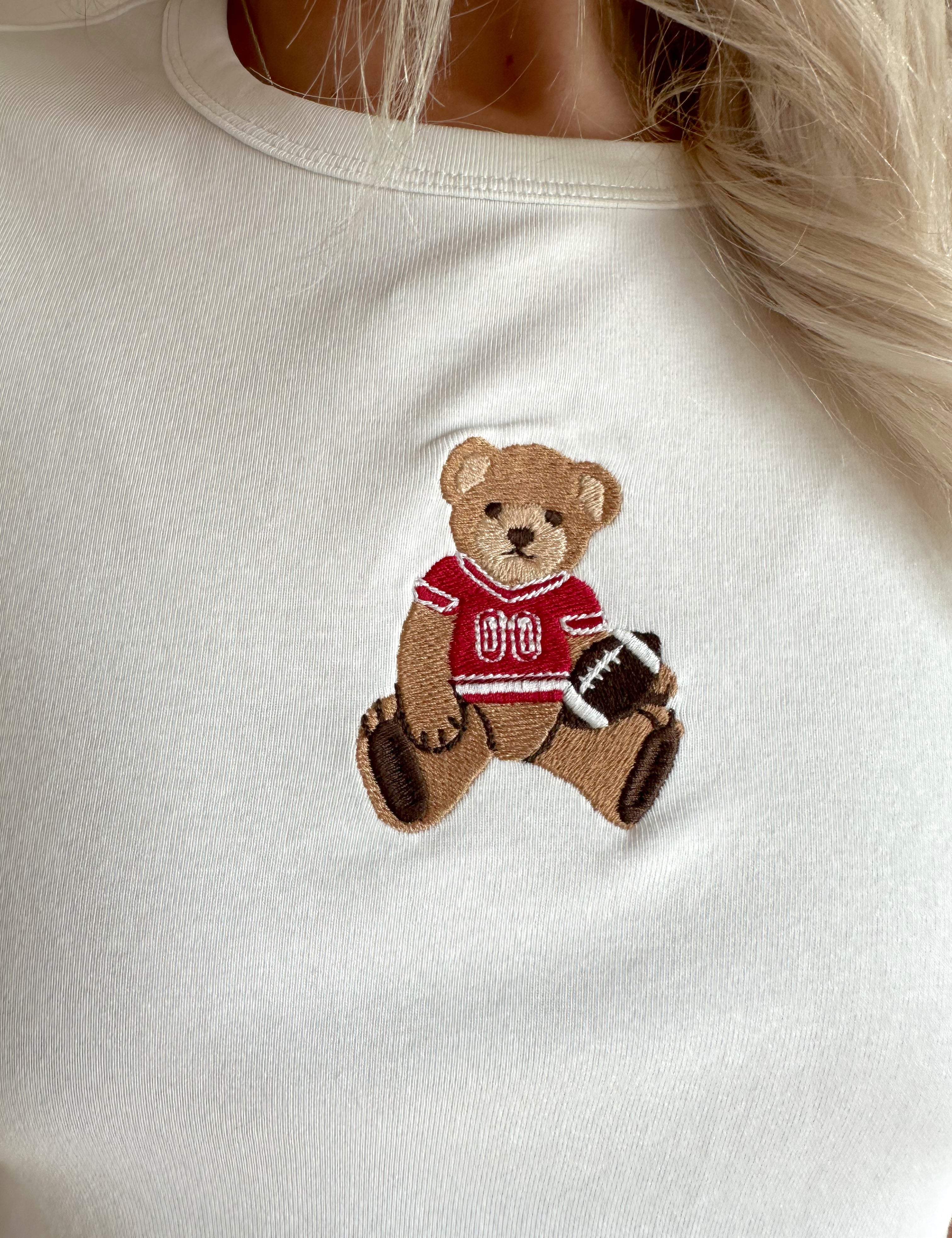 Woman wearing a white cropped t-shirt with embroidered teddy bear and cream mini skirt. 