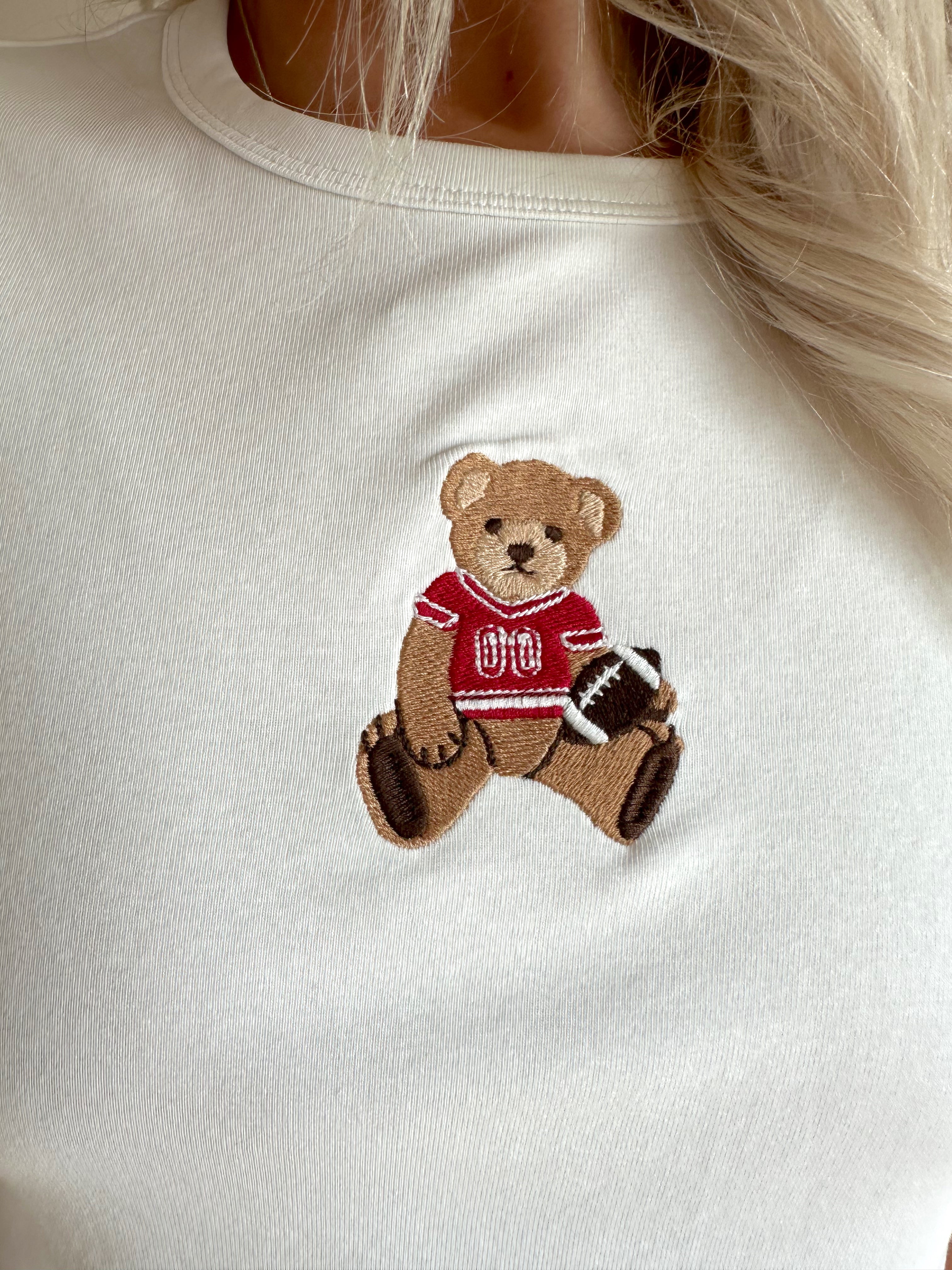 Woman wearing a white cropped t-shirt with embroidered teddy bear and cream mini skirt. 