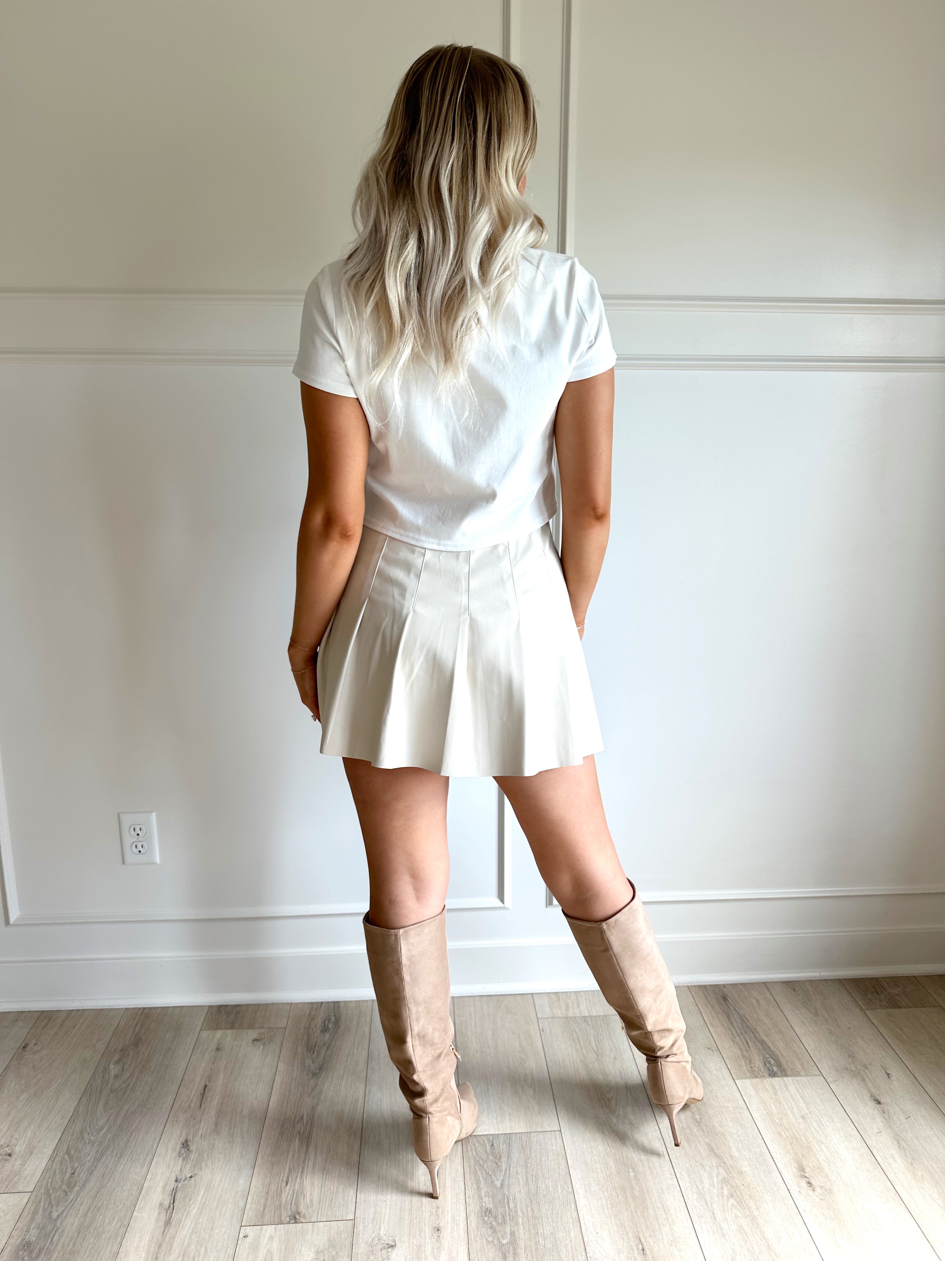 Woman wearing a white cropped t-shirt with embroidered teddy bear and cream mini skirt. 