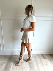 Woman wearing a white cropped t-shirt with embroidered teddy bear and cream mini skirt. 