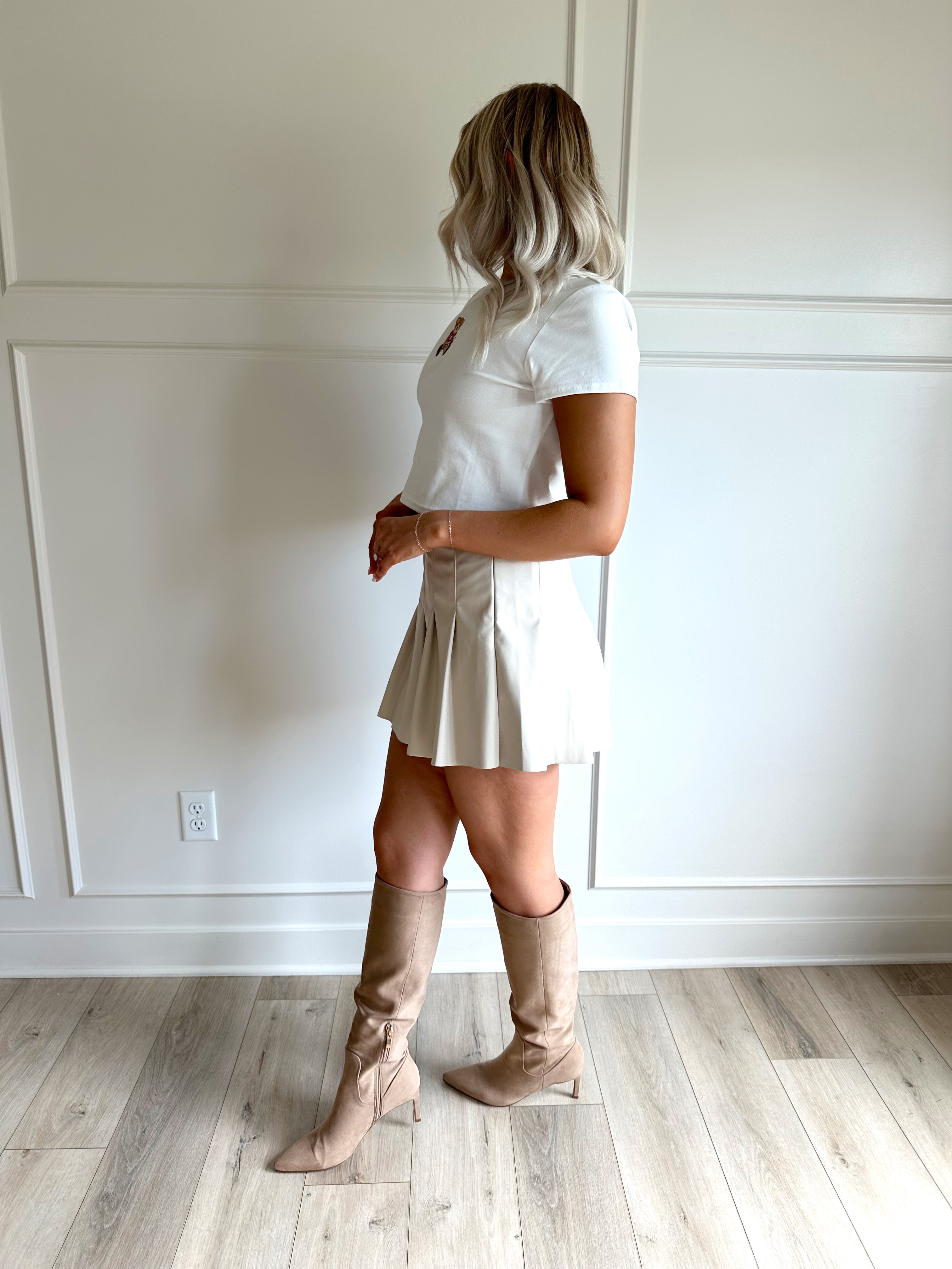Woman wearing a white cropped t-shirt with embroidered teddy bear and cream mini skirt. 