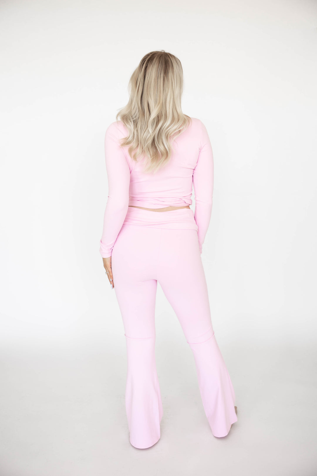 Woman wearing light pink two piece yoga set with wrap top, and fold over pant. 