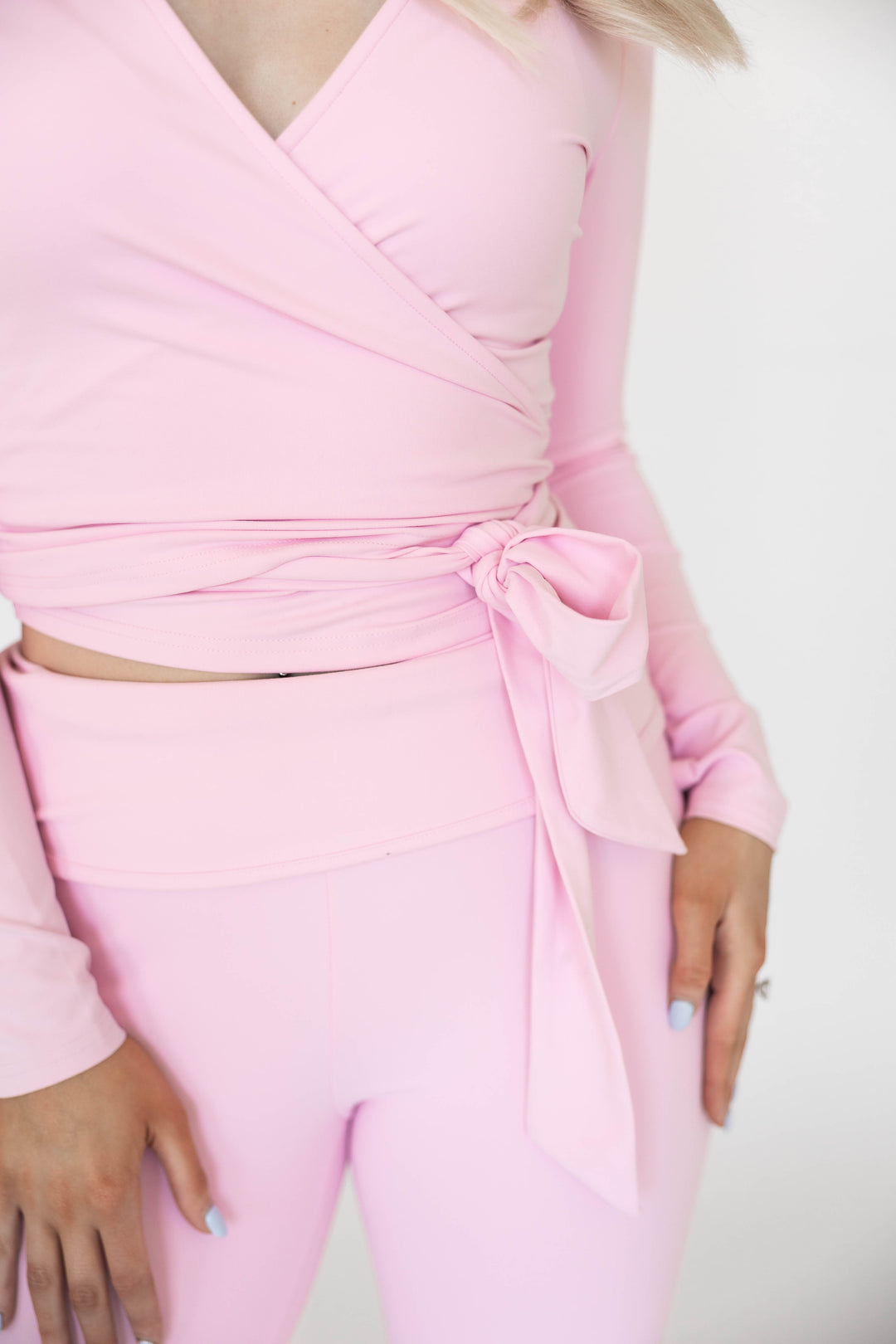 Woman wearing light pink two piece yoga set with wrap top, and fold over pant. 
