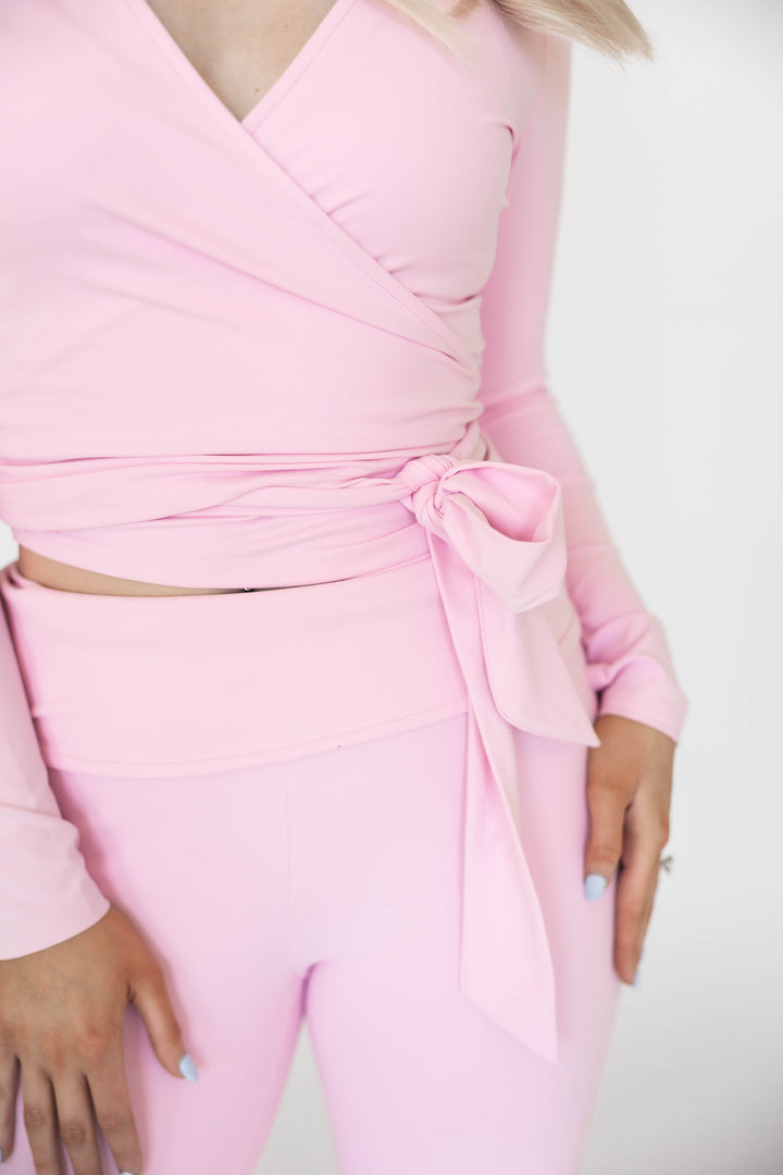Woman wearing light pink two piece yoga set with wrap top, and fold over pant. 