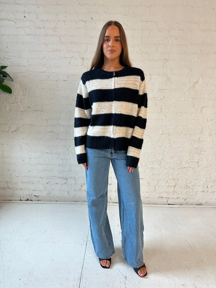 Woman wearing navy and ivory chunky striped knit jacket with medium wash jeans. 