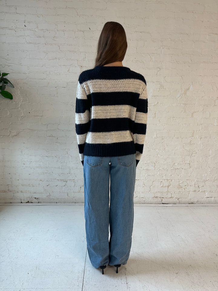 Woman wearing navy and ivory chunky striped knit jacket with medium wash jeans. 