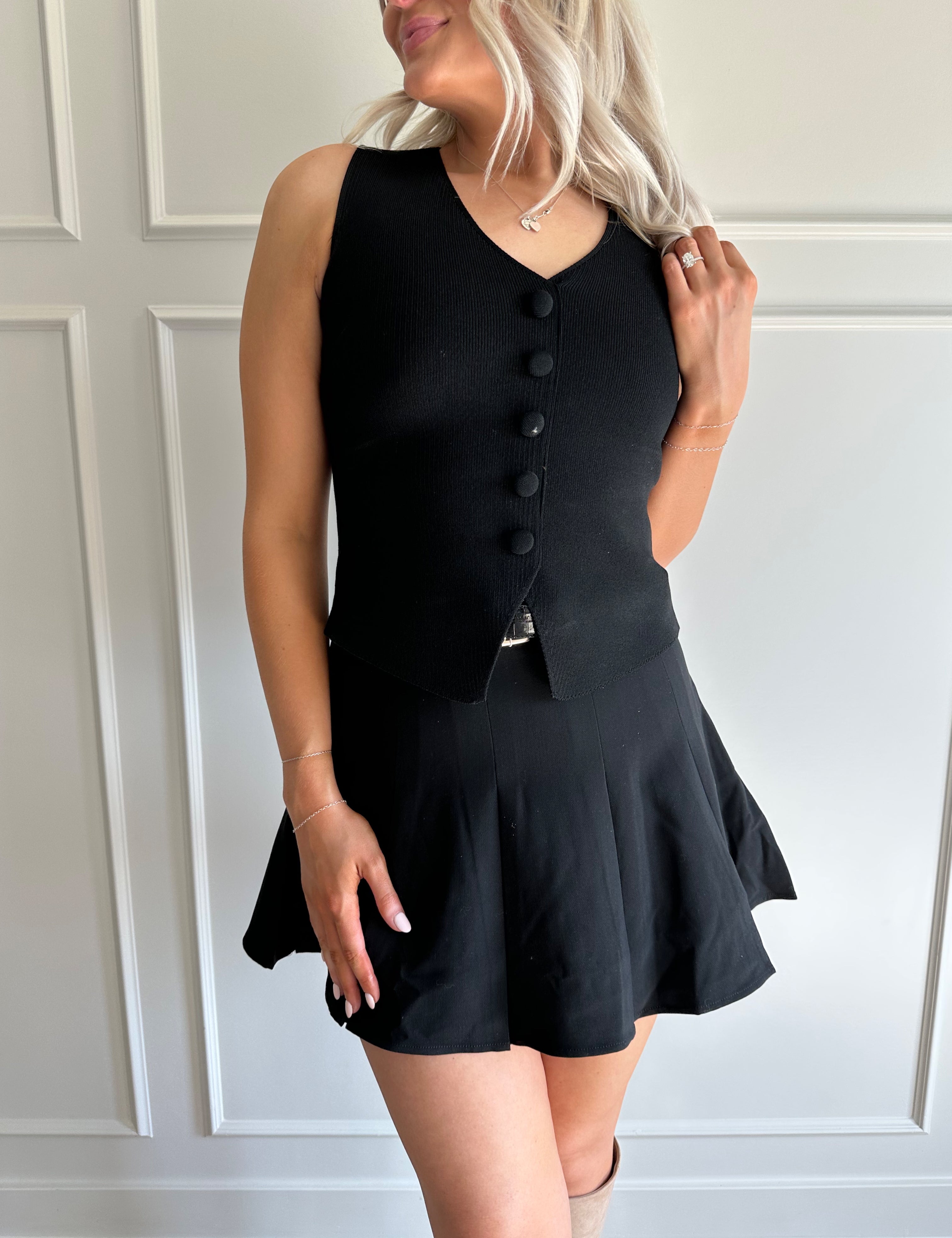 Woman wearing black tailored vest top with button detailing. 