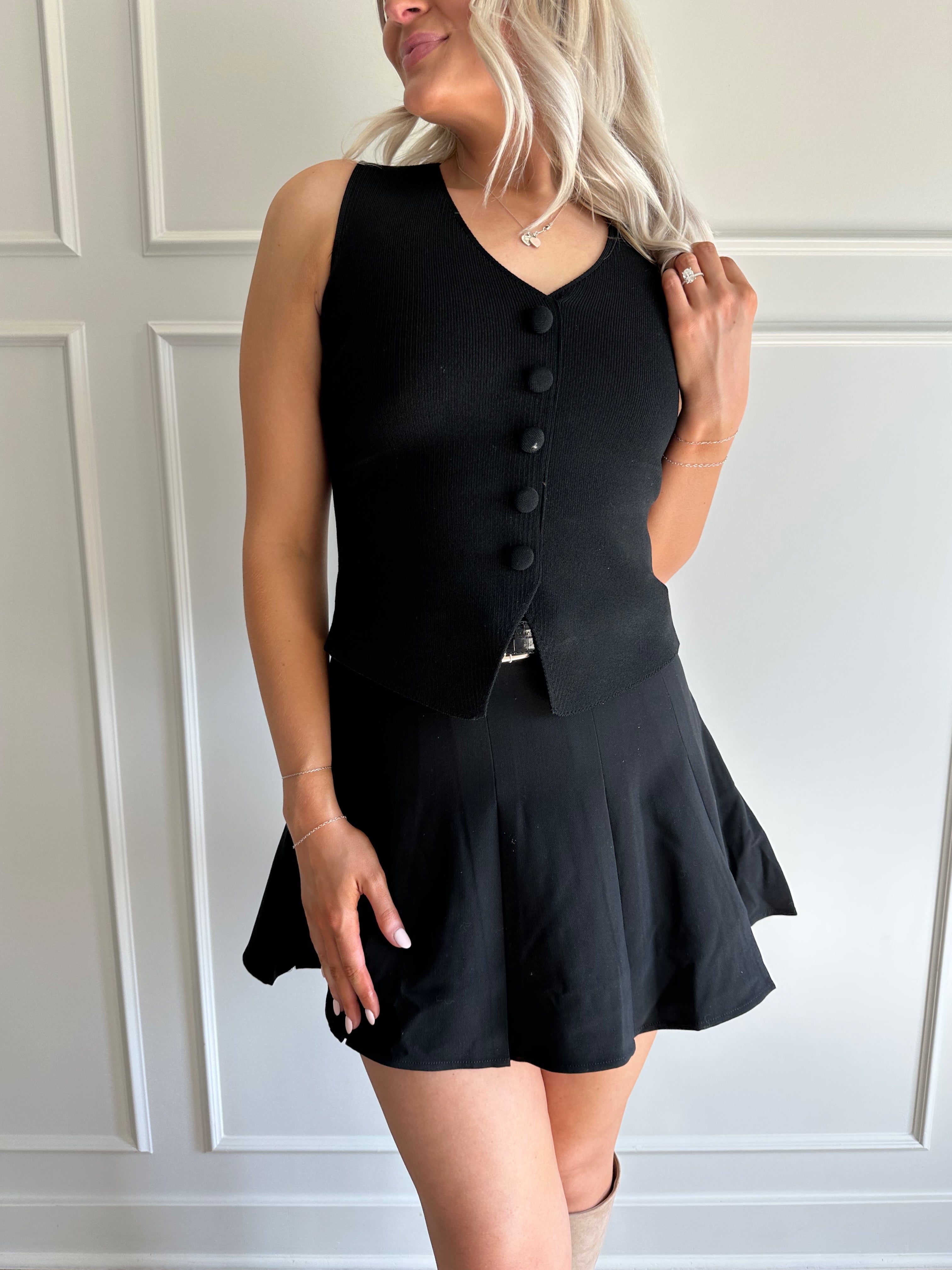 Woman wearing black tailored vest top with button detailing. 