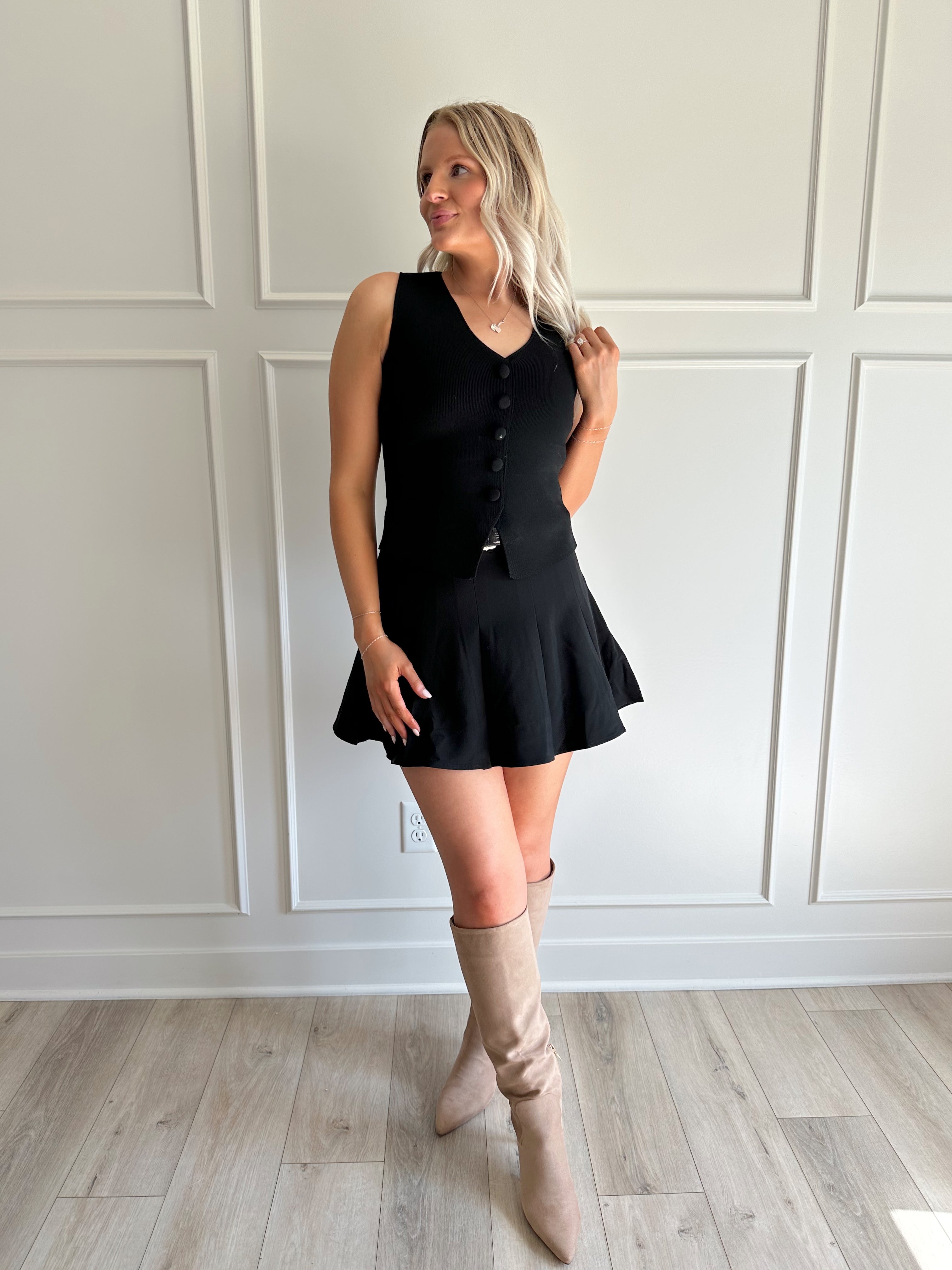 Woman wearing black tailored vest top with button detailing. 