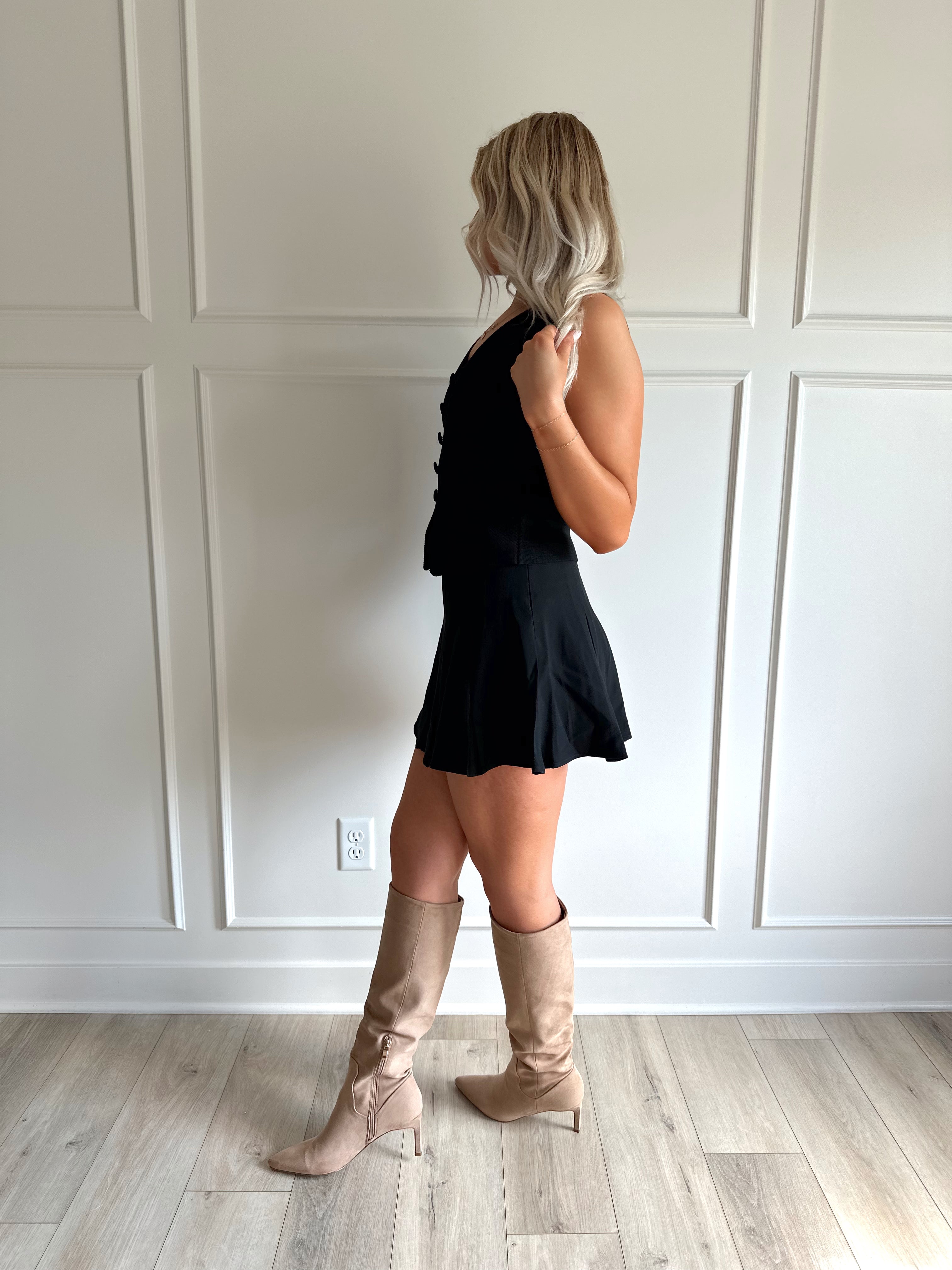 Woman wearing black tailored vest top with button detailing. 