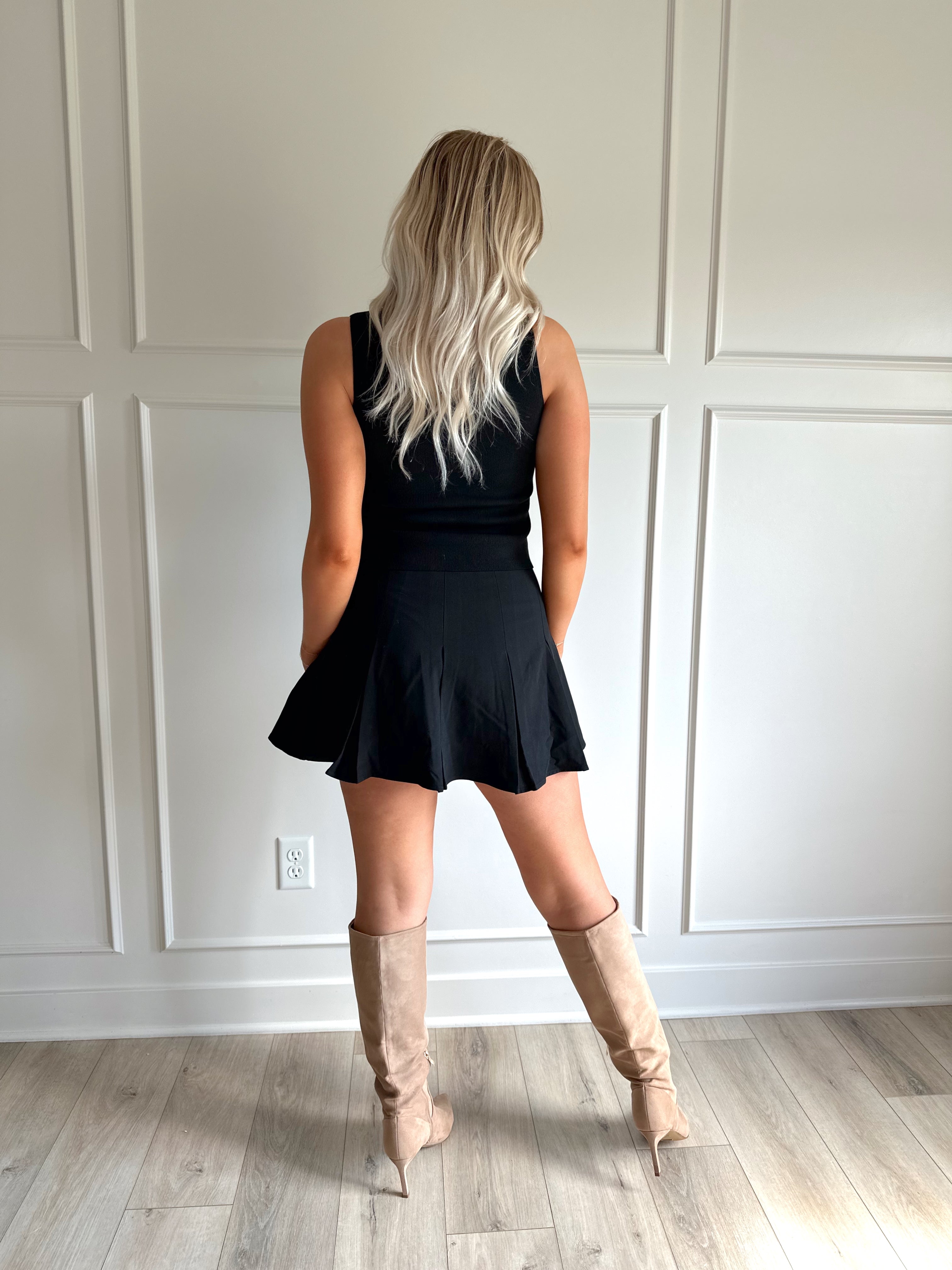 Woman wearing black tailored vest top with button detailing. 