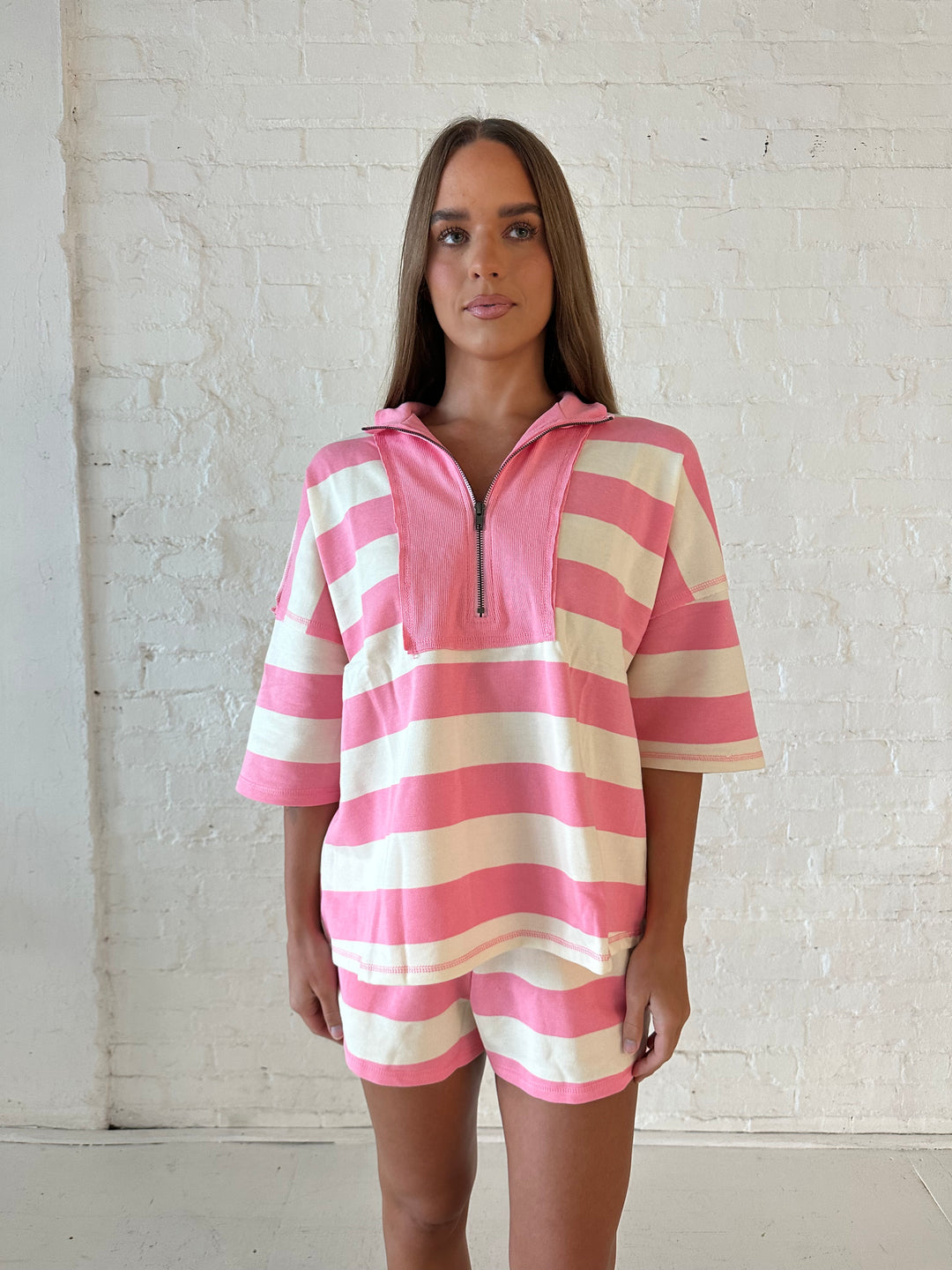 Woman wearing pink and white striped two piece lounge set and flip flops. 