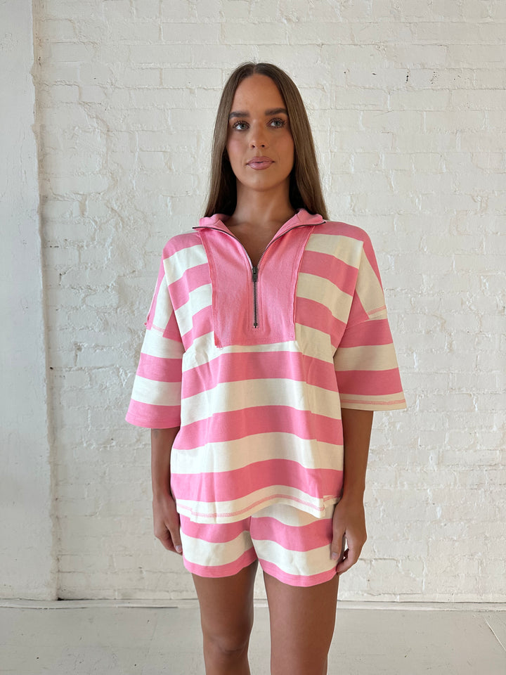 Woman wearing pink and white striped two piece lounge set and flip flops. 