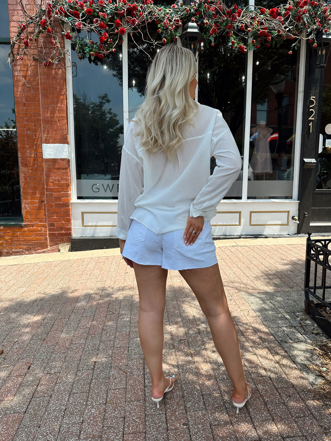 Woman wearing white denim shorts with a raw hem, and a button up white short.
