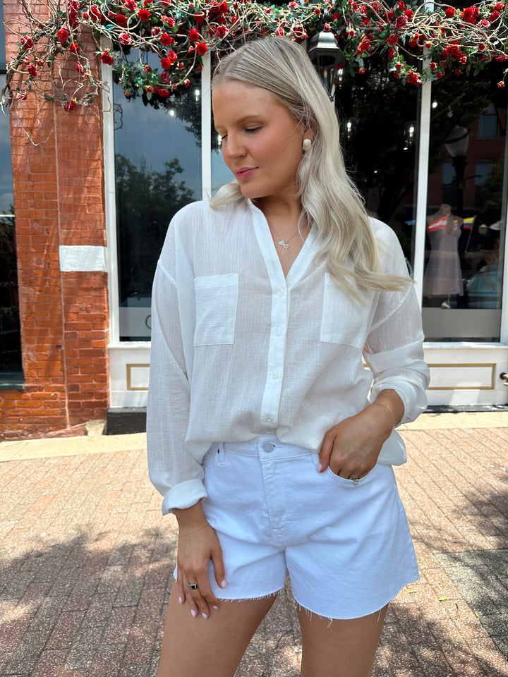 Woman wearing white denim shorts with a raw hem, and a button up white short.
