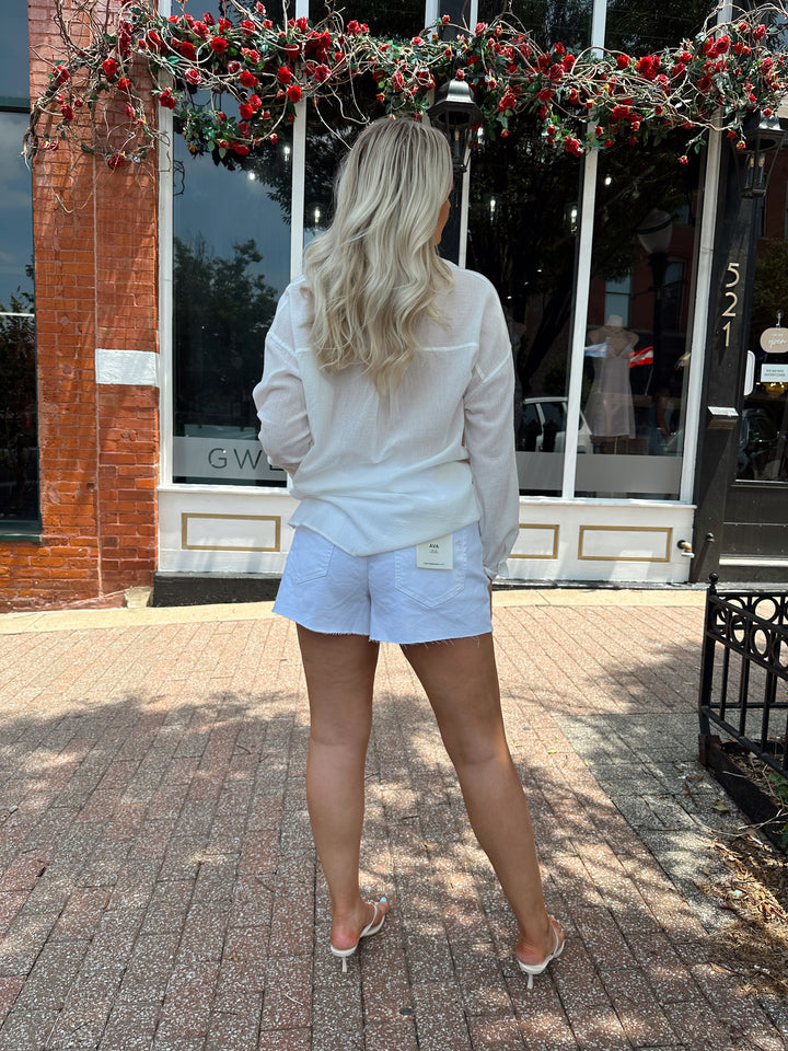 Woman wearing white denim shorts with a raw hem, and a button up white short.