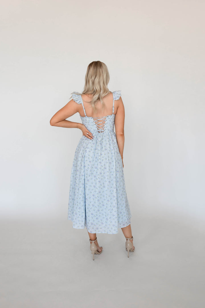Woman wearing blue eyelet floral midi dress with corset back and side slit. 