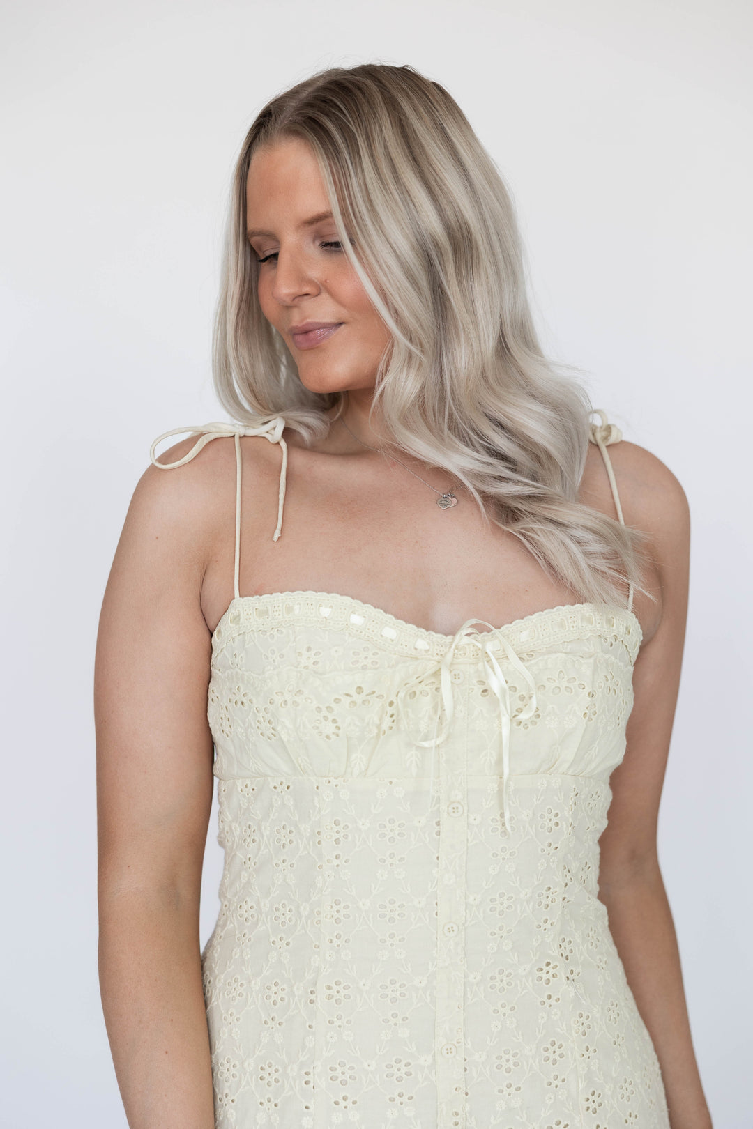 Woman wearing light yellow eyelet mini dress with ribbon detailing. 
