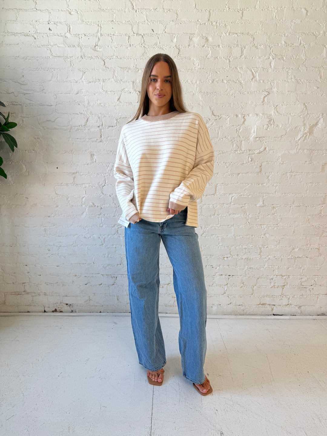 Woman wearing beige and ivory striped pull over sweater with medium wash jeans. 