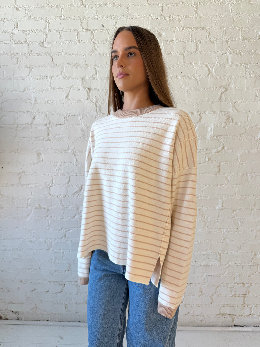 Woman wearing beige and ivory striped pull over sweater with medium wash jeans. 