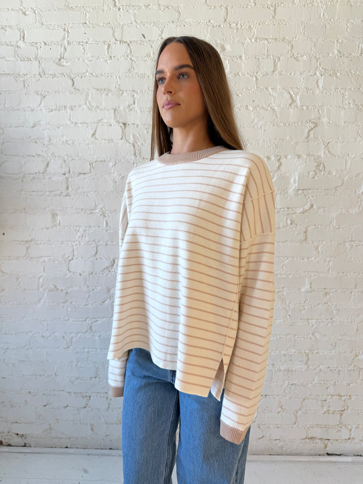 Woman wearing beige and ivory striped pull over sweater with medium wash jeans. 