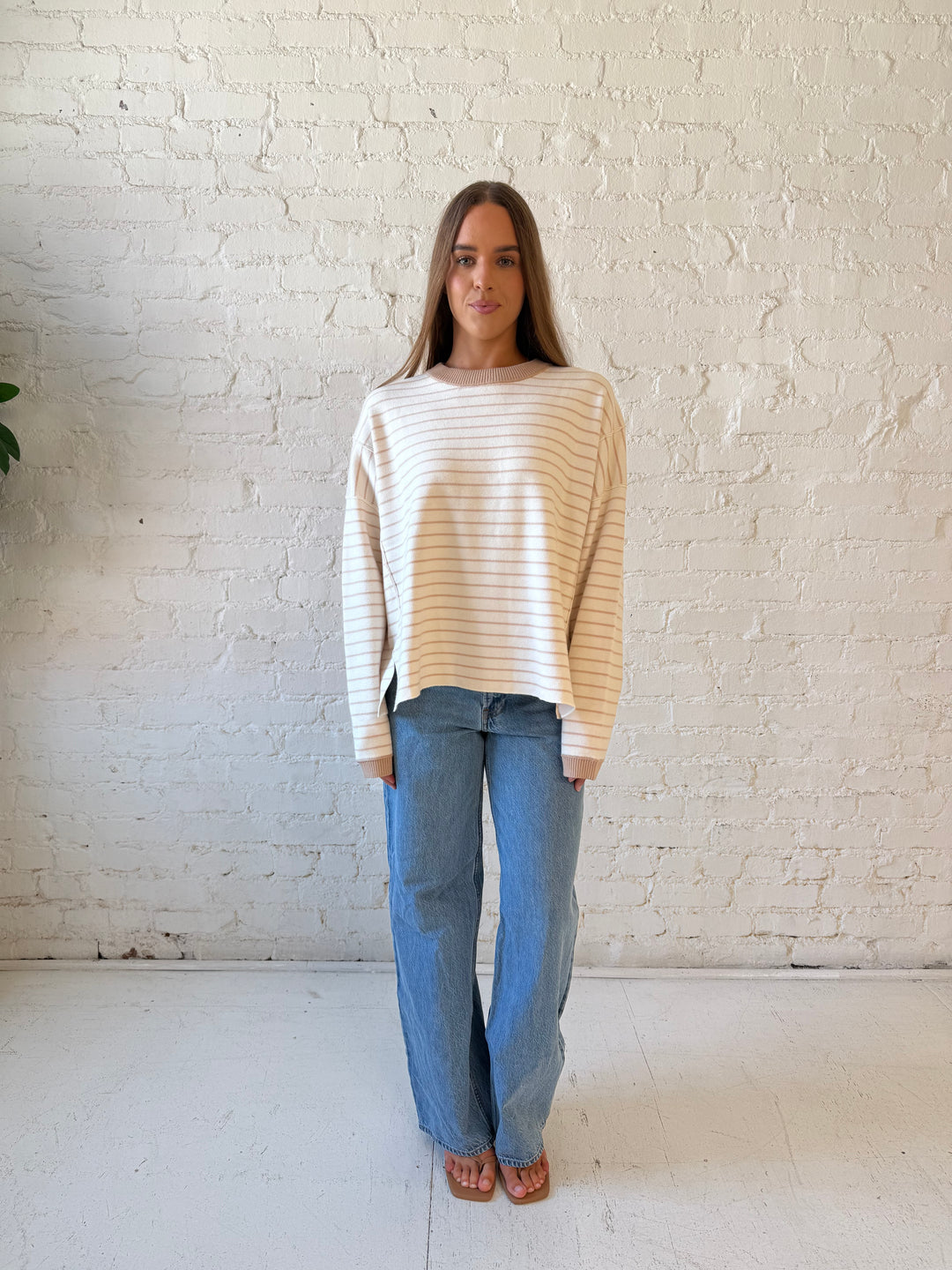 Woman wearing beige and ivory striped pull over sweater with medium wash jeans. 