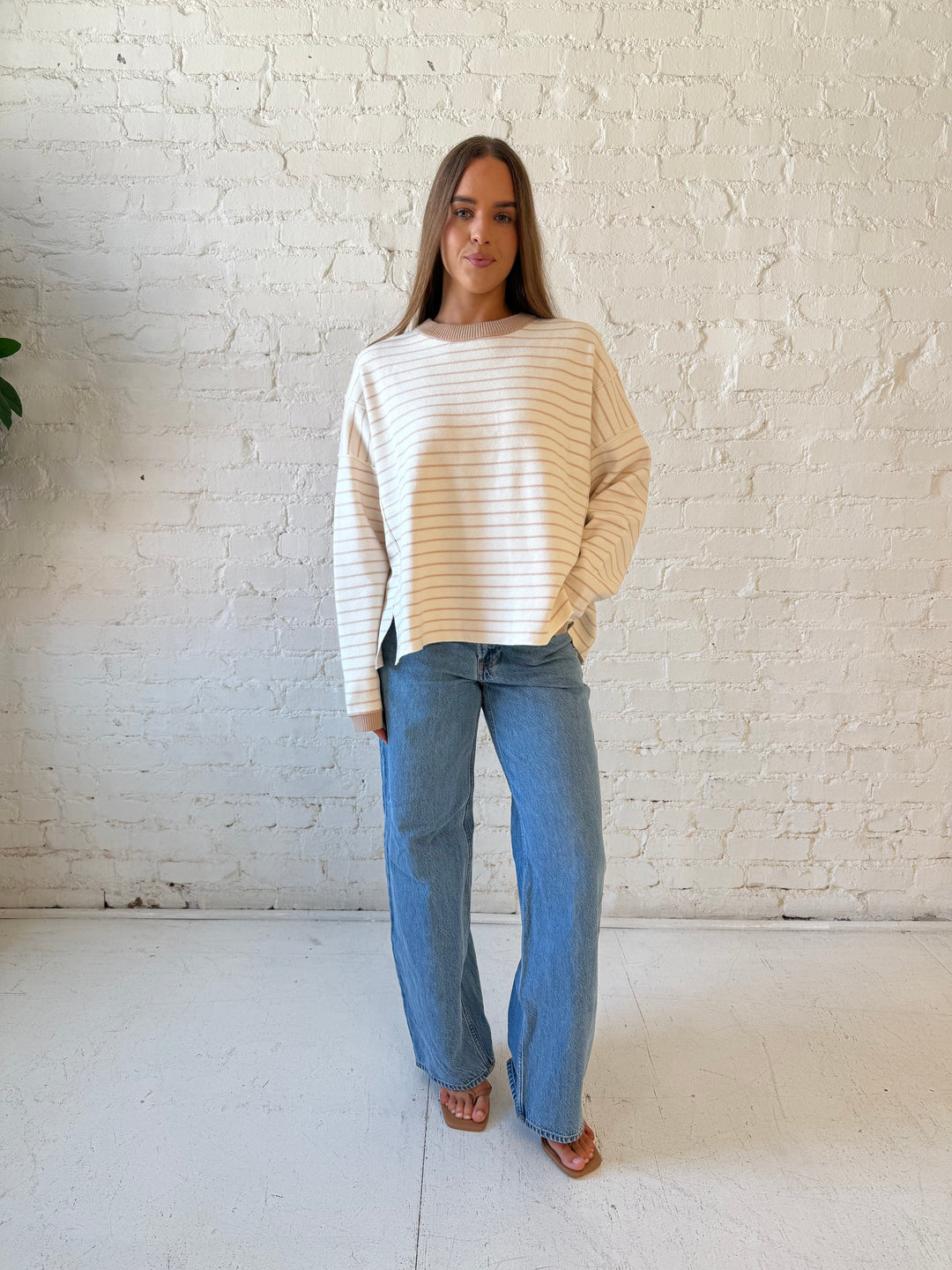 Woman wearing beige and ivory striped pull over sweater with medium wash jeans. 