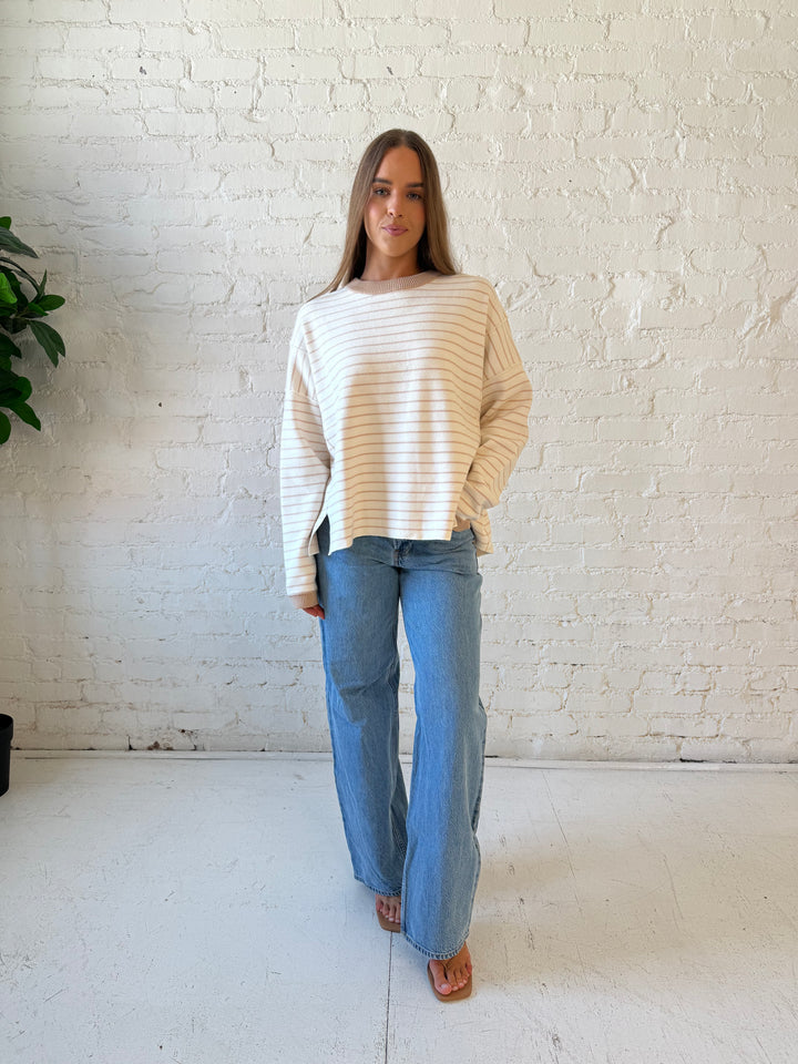 Woman wearing beige and ivory striped pull over sweater with medium wash jeans. 