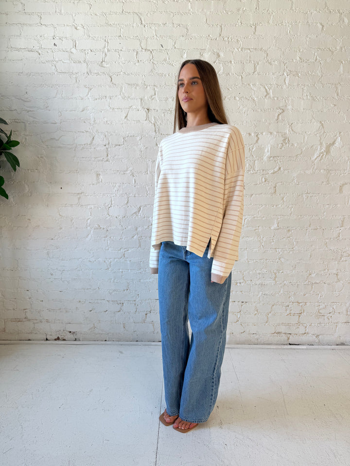 Woman wearing beige and ivory striped pull over sweater with medium wash jeans. 