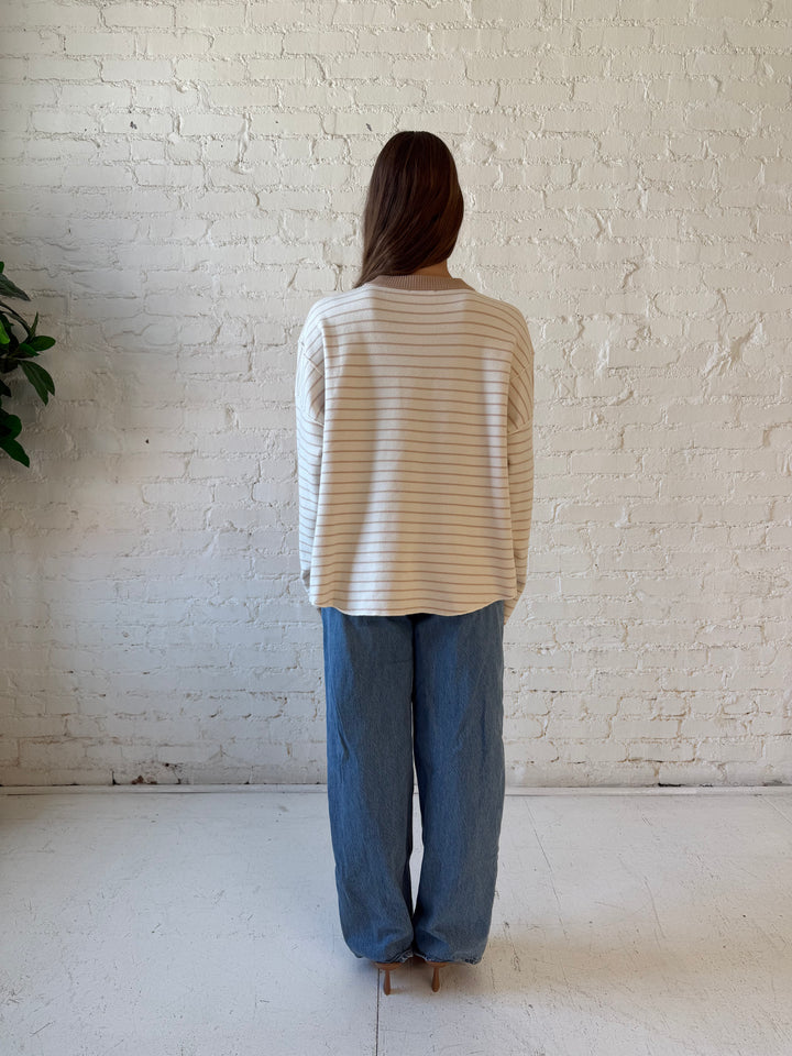 Woman wearing beige and ivory striped pull over sweater with medium wash jeans. 