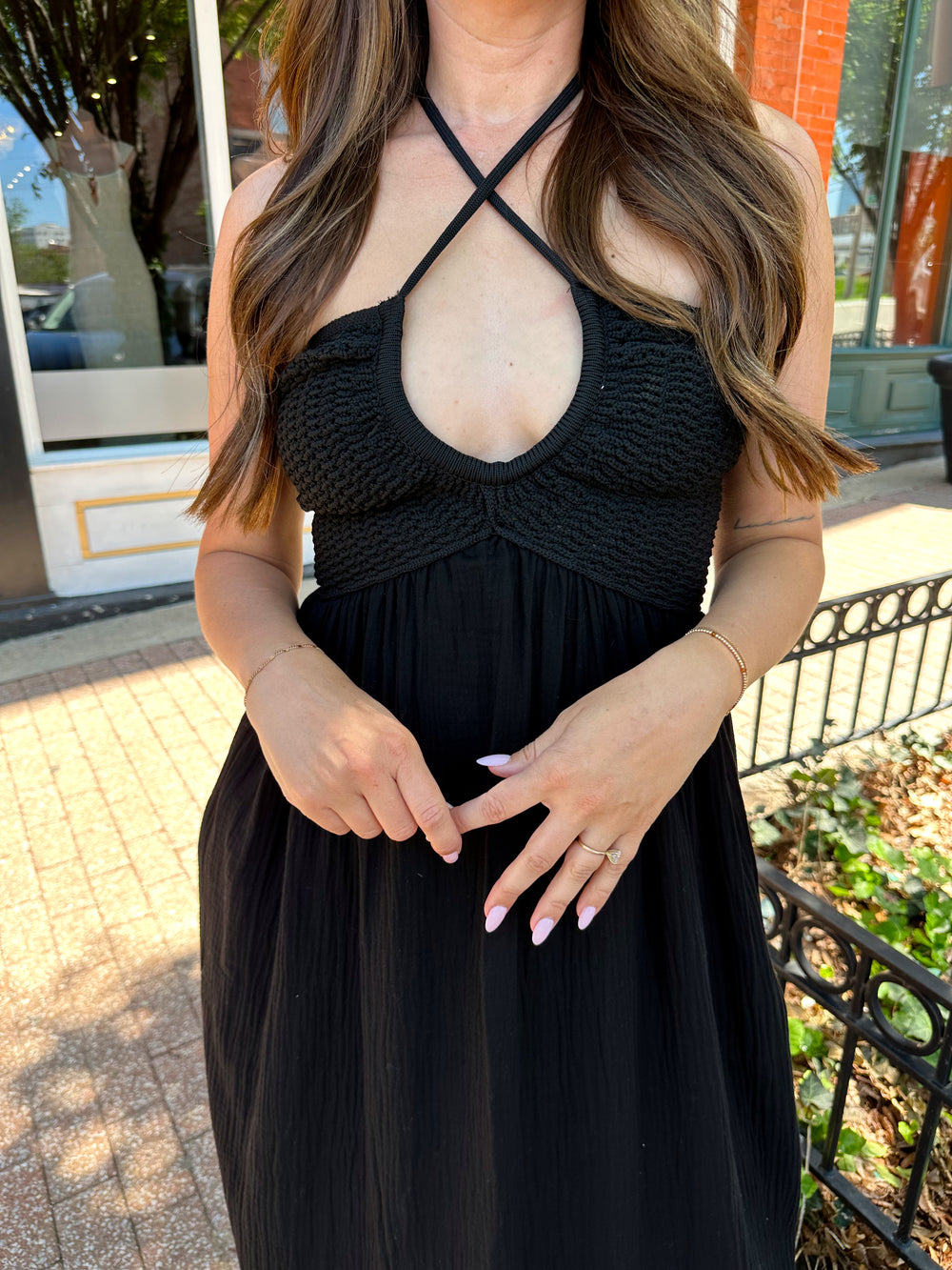 Woman wearing black contrast midi dress with a crochet criss cross halter top, and gauze bottom.