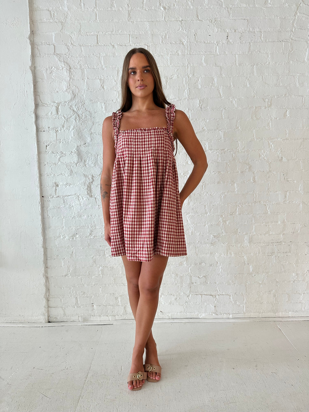 Woman wearing red and beige plaid babydoll style mini dress with gathered neckline, and gathered straps.