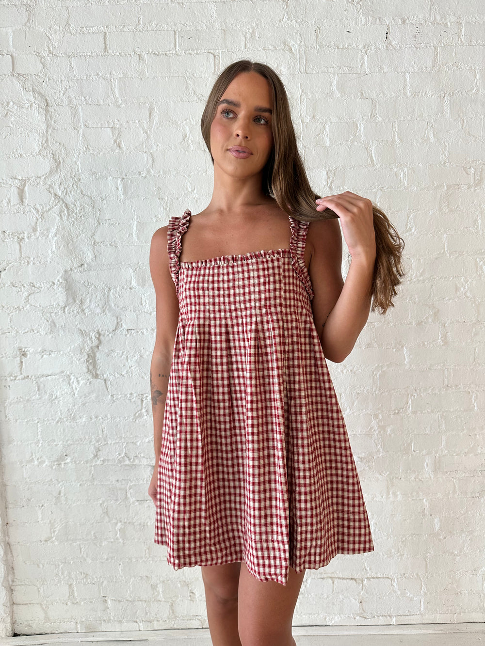 Woman wearing red and beige plaid babydoll style mini dress with gathered neckline, and gathered straps.