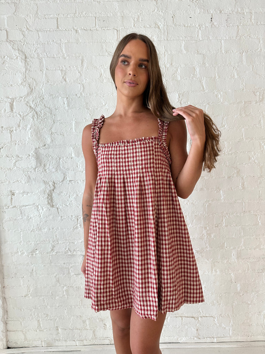 Woman wearing red and beige plaid babydoll style mini dress with gathered neckline, and gathered straps.