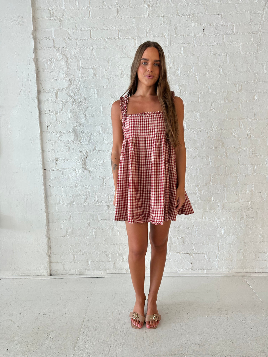Woman wearing red and beige plaid babydoll style mini dress with gathered neckline, and gathered straps.